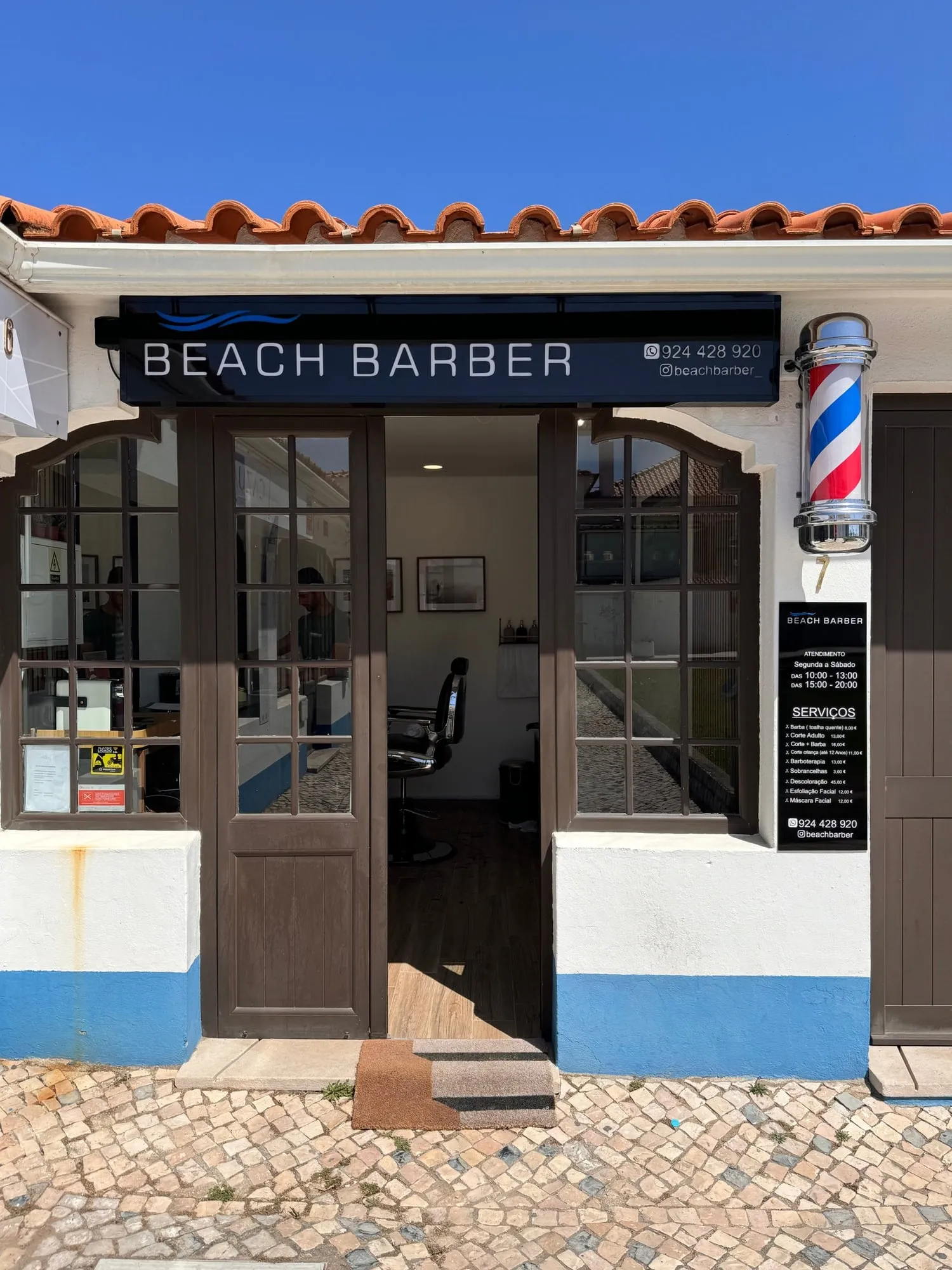 A fachada da Beach Barber: casa branca com barra azul, porta de madeira e poste de barbeiro